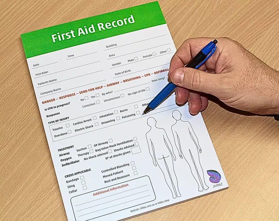 A4 First Aid Checklist notepad with hardback cover with hand completing checks, open to show structured prompts and checkboxes